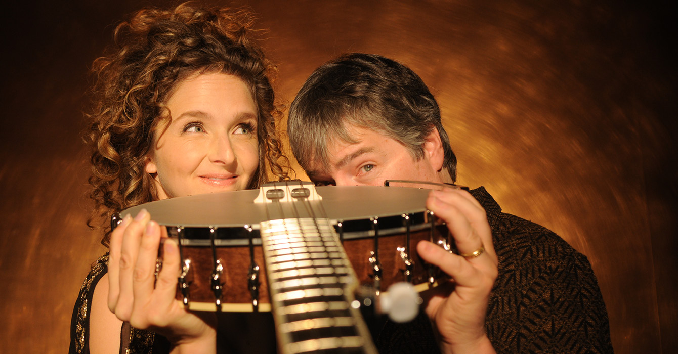 Bela Fleck and Abigail Washburn pose, peering over a banjo in their hands on a brown background